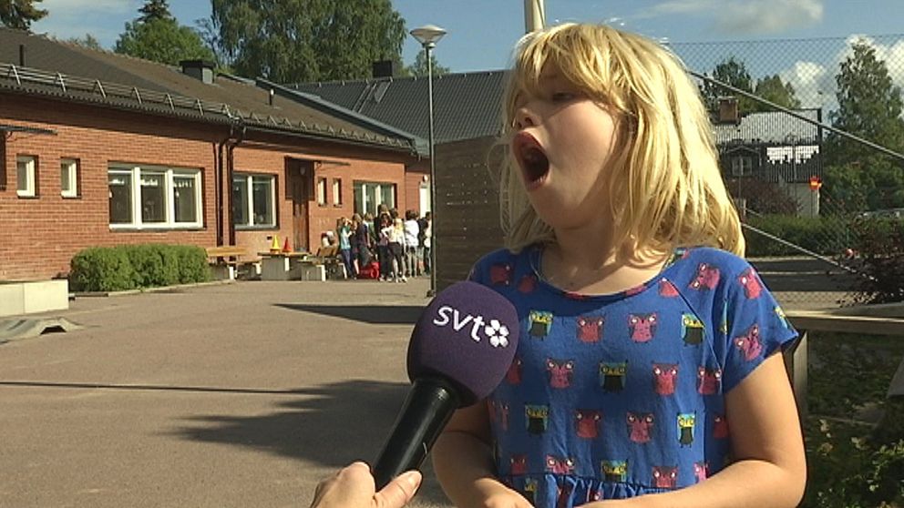 ung flicka intervjuas på skolgård, grimaserar med öppen mun