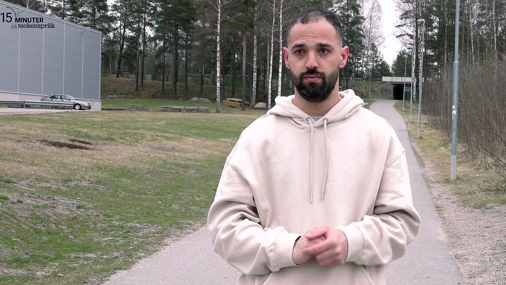 Maruf Mohammadi i beige hoodie står på gångväg i utomhusmiljö med träd i bakgrunden.