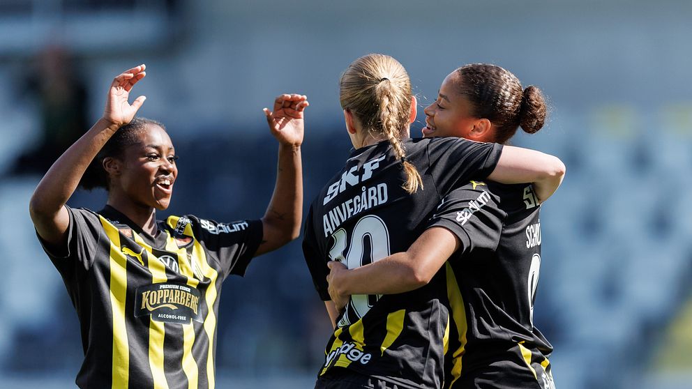 Tre fotbollsspelare i svartgula matchställ firar tillsammans på planen.