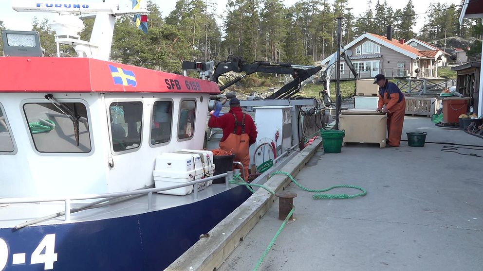 Två fiskare står vid en fiskebåt i Bondhamn