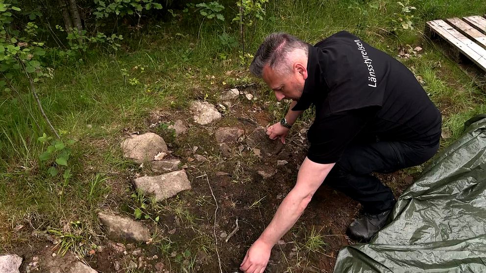 medelålders man i svart tröja som det står länsstyrelsen på undersöker en gammal grav