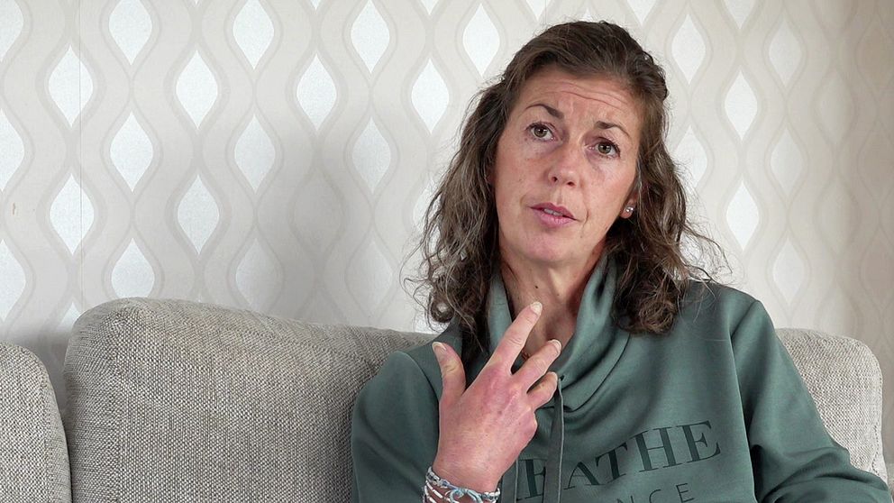Kvinna med brunt hår och grön luvtröja sitter i soffa