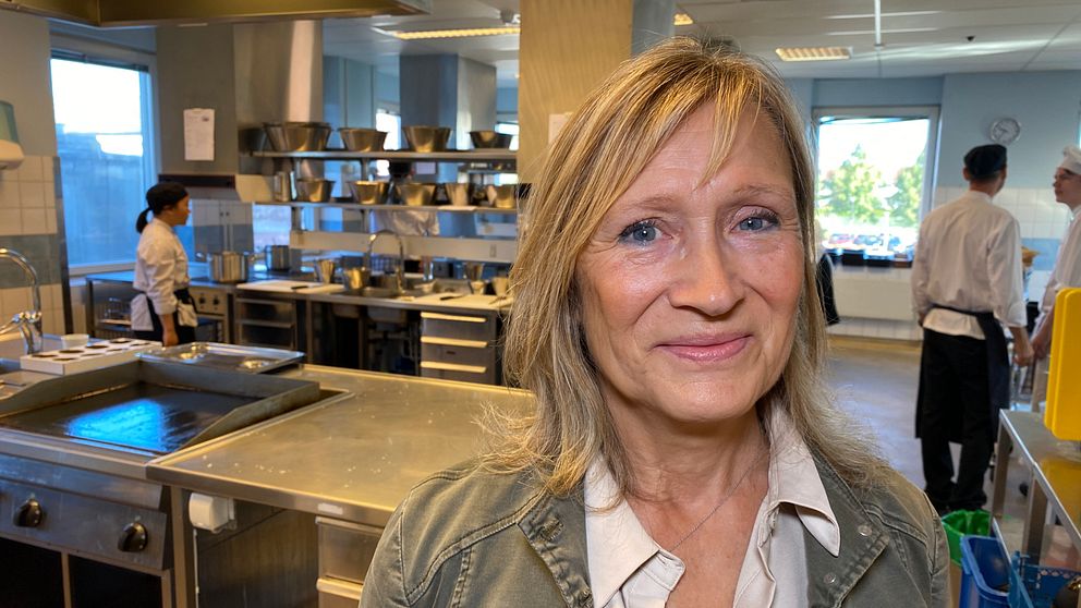 Åsa Ersson, biträdande rektor på Lindengymnasiet i Katrineholm, står i restaurangköket. I bakgrunden står kockelever och lagar mat.