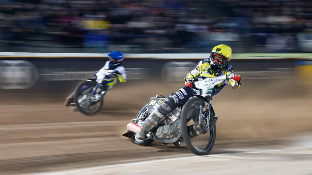 Två speedwaymotorcyklar med förare. Sanden yr.