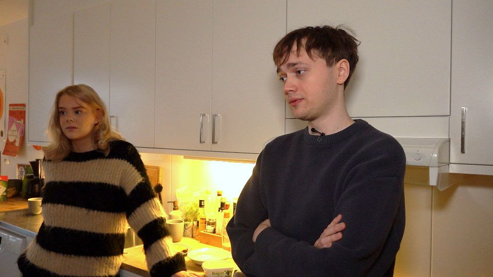 Ungt par som står i ett kök. De kämpar med sin dyra nyproducerade lägenhet i Stockholm.