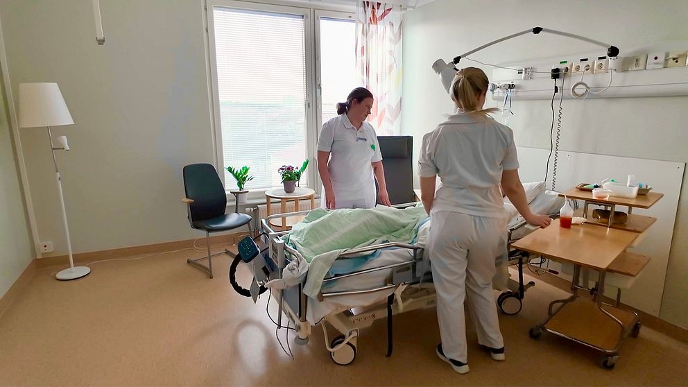 Två sjuksköterskor vårdar en patient i ett sjukhusrum med utrustning.