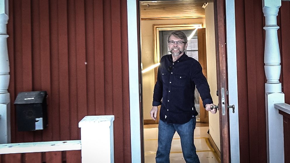 en man öppnar en dörr på ett falurödfärgat hus.