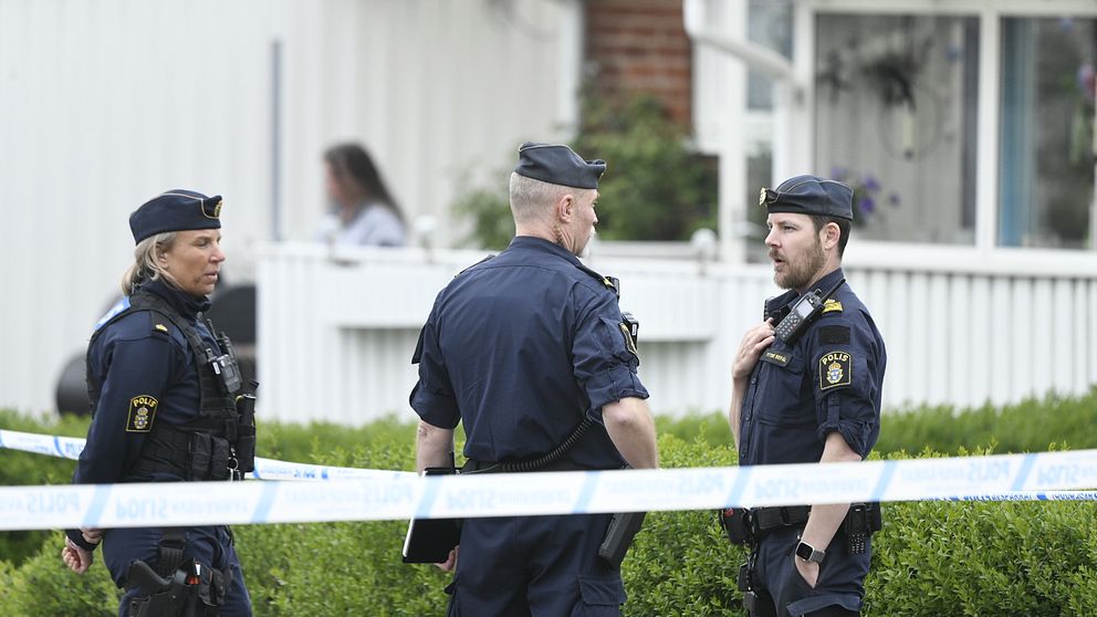 Tre poliser samtalar vid avspärrning utanför ett bostadshus i Klippan, kvinna syns i bakgrunden.