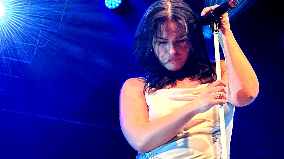 Molly Hammar i vit klänning uppträder på Kulturskolans scen i Sandviken med mikrofon under blå scenbelysning