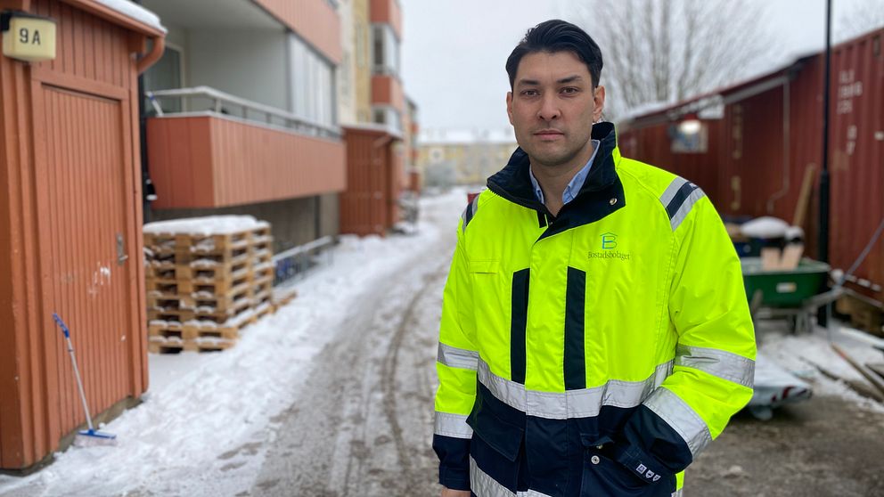 Man i varseljacka med svart hår står utanför lägenhetshus på Tunet i Mjölby