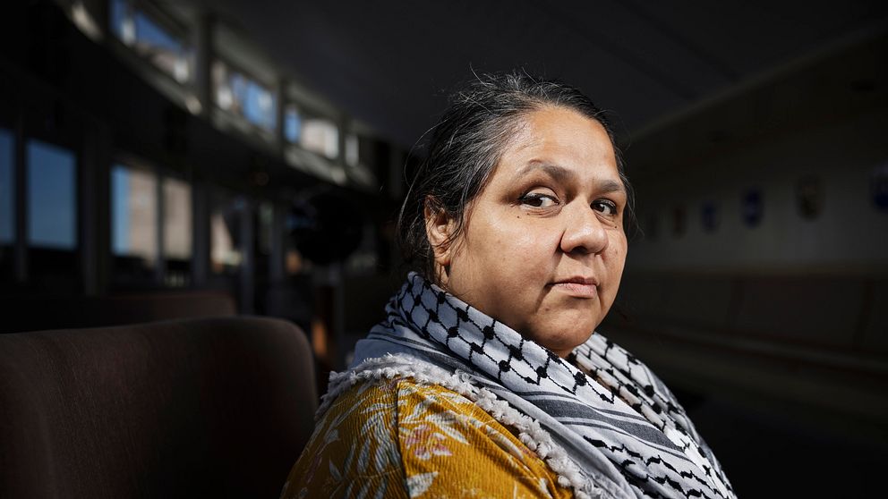 Person med palestinasjal sitter i ett svagt upplyst rum.