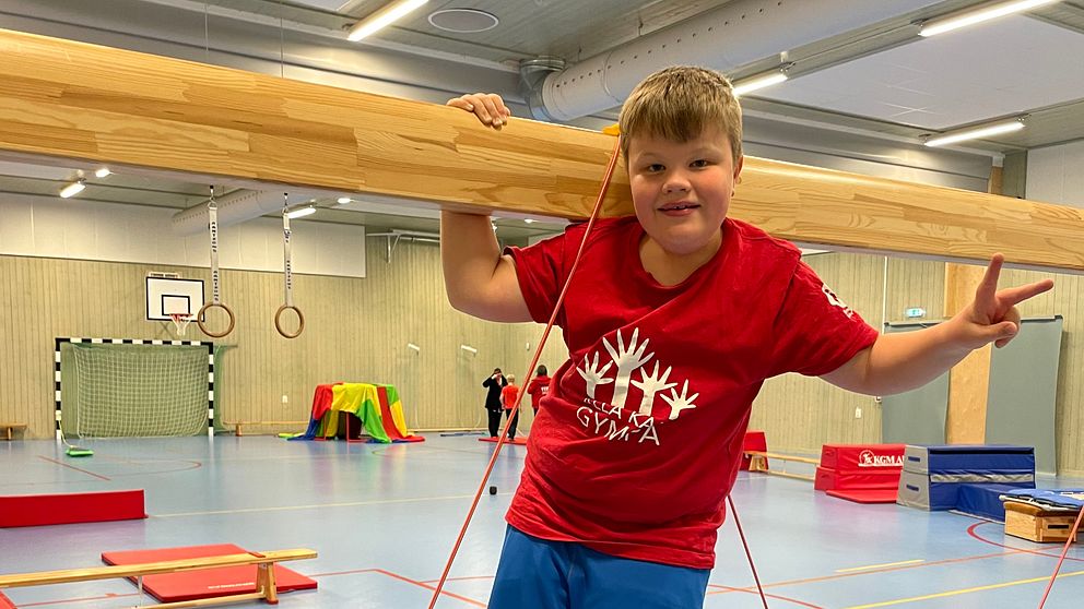 Barn i röd tröja i gymnastiksal med redskap och hinderbanor.