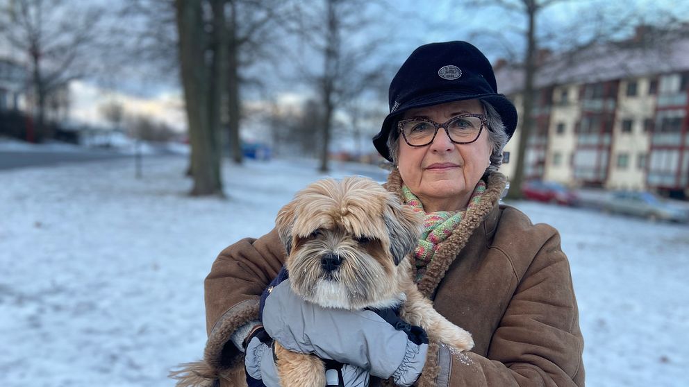 Kvinna står utomhus med liten hund i famnen.