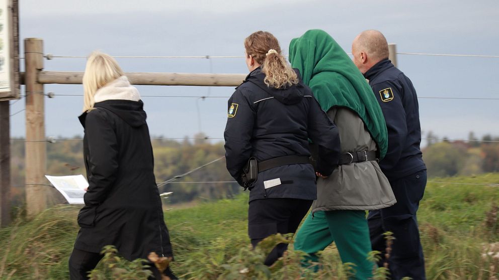 den misstänkta går med vakter runt området där den misstänkta brottsplatsen är.