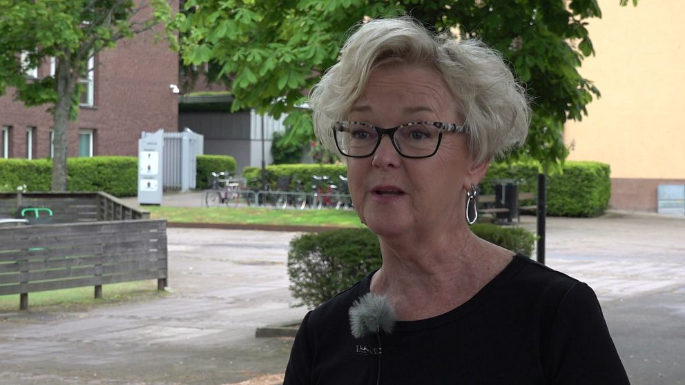 Kvinna intervjuas utomhus i ett bostadsområde med träd och byggnader i bakgrunden.