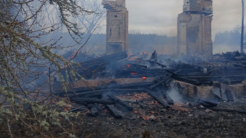 Två skorstenar står kvar efter en brand, omgivna av rök och förkolnade rester.
