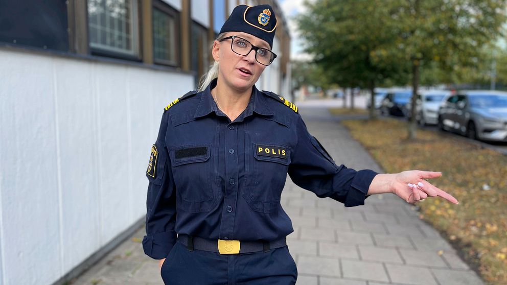 En polis i uniform står på en gata och pekar med ena handen, med träd och parkerade bilar i bakgrunden. Tina Anderberg. Våld i nära relationer.