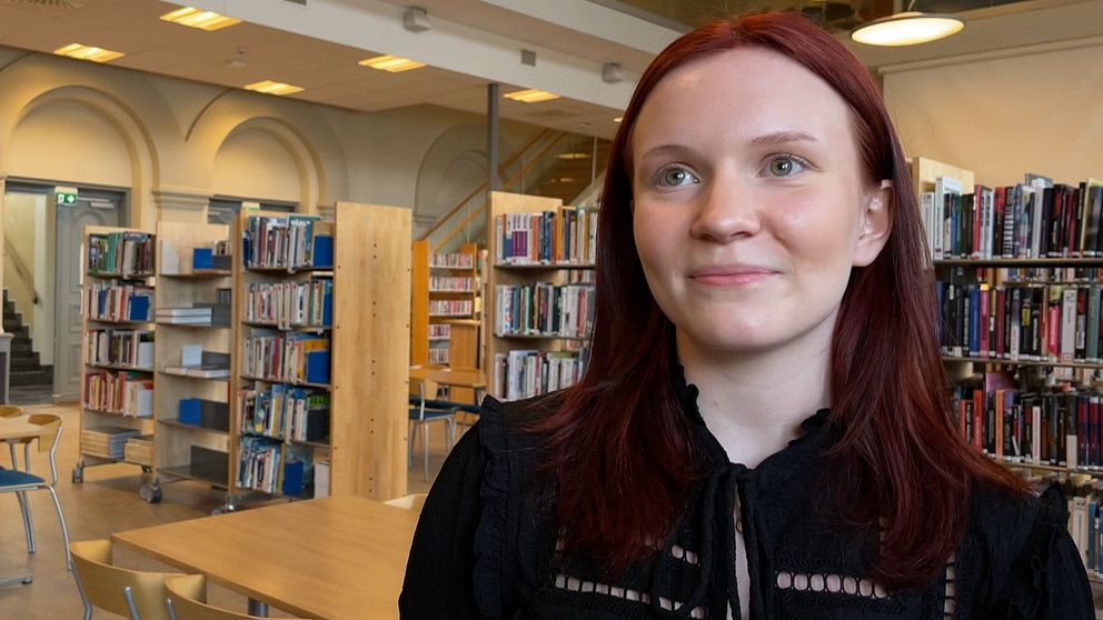 Person står framför bokhyllor i ett bibliotek med klassisk inredning.