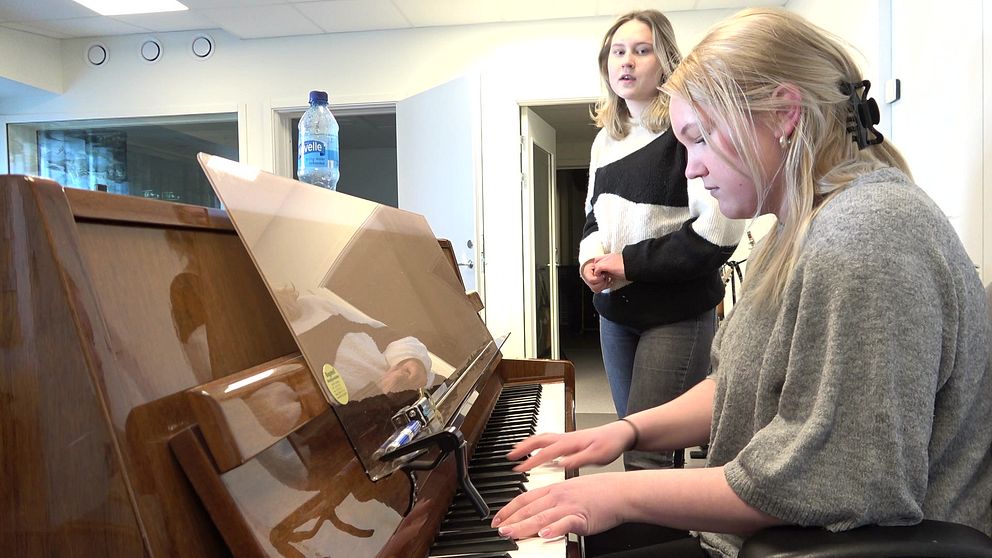 Två tjejer vid ett piano. En spelar och en sjunger.