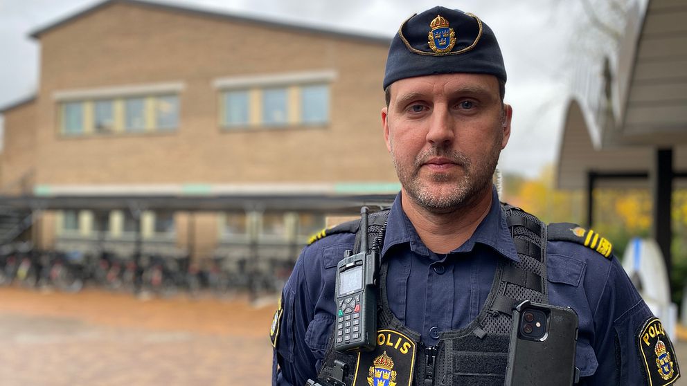 Polis i uniform står framför en tegelbyggnad.