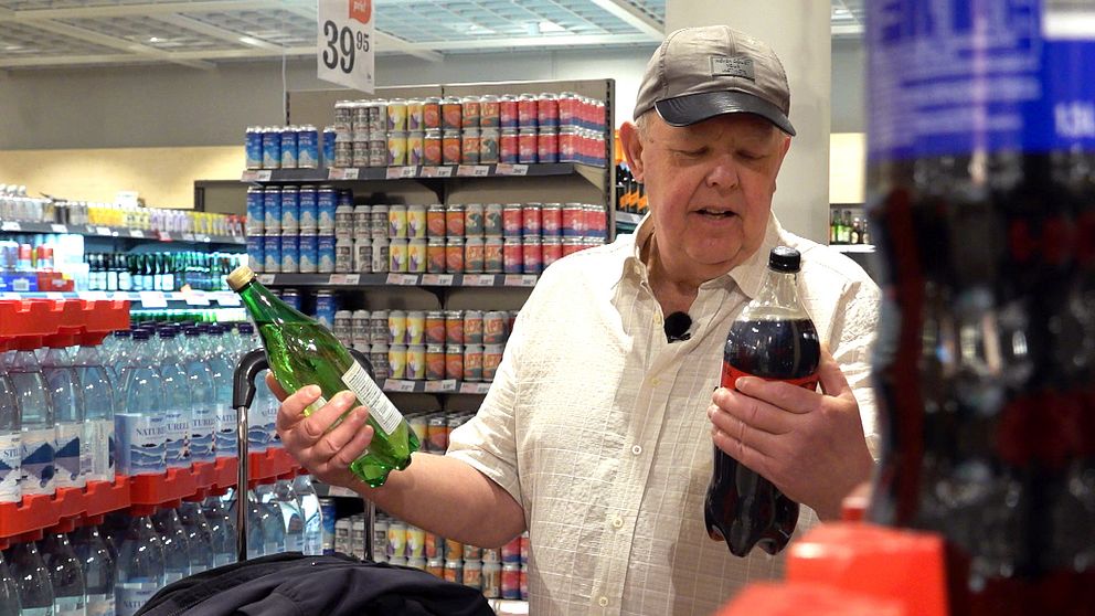 Person i butik väljer mellan två flaskor, en grön glasflaska och en svart plastflaska.