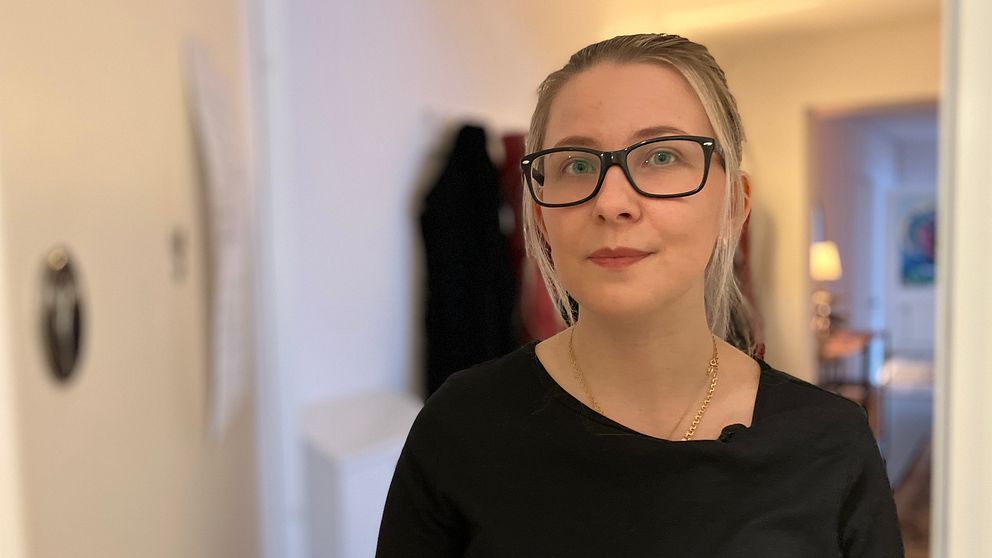 Blond tjej med glasögon står i en dörröppning och tittar rakt in i kameran