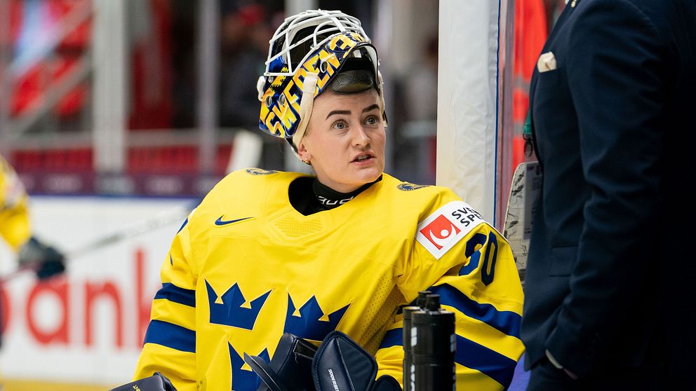Hockeyspelare i gula tröjor vid rinken. Coach talar med en målvakt.