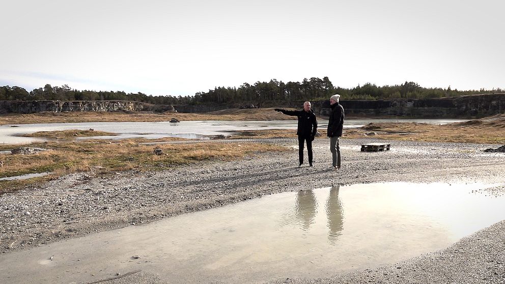 Två män står och pekar i ett gammalt stenbrott i Hejdeby