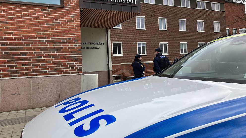 Polisbil i förgrunden. Kalmar tingsrätt i bakgrunden. Två poliser står och pratar.