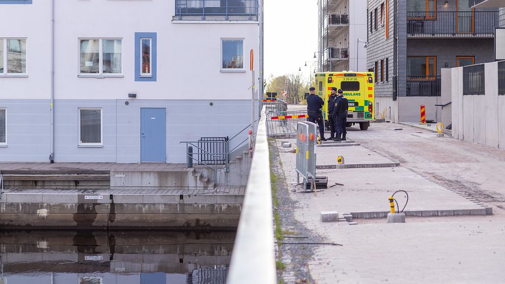 Ambulans och polis på gata vid bostadshus nära vattnet.