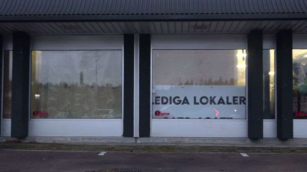 Skyltfönster med texten ”Lediga lokaler” i vit och svart färg, delvis täckt av smutsiga eller träningsskyddade fönster. Bakom fönstret syns suddiga konturer av vad som troligen är inredning eller föremål i lokalen.