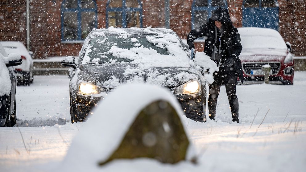 kvinna som borstar av snöig bil