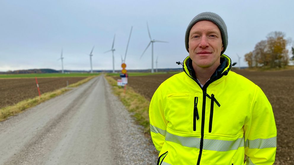 Man i gula varselkläder vid en väg. Vindkraftverk i bakgrunden