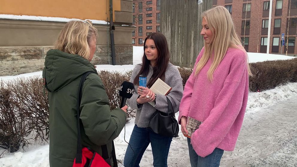 En reporter från SVT intervjuar två personer utomhus på en snöig trottoar. Personen som håller mikrofonen är klädd i en grön jacka och de två intervjupersonerna har på sig vinterkläder, inklusive en grå och en rosa tröja. I bakgrunden syns byggnader.