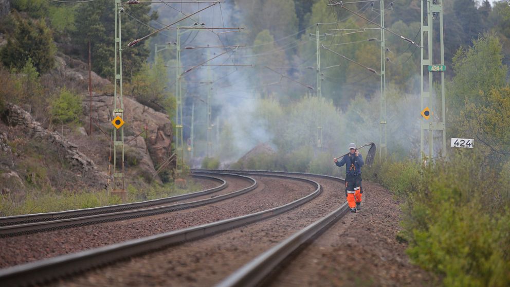 En brandman går på ett järnvägsspår, i bakgrunden ser man brandrök