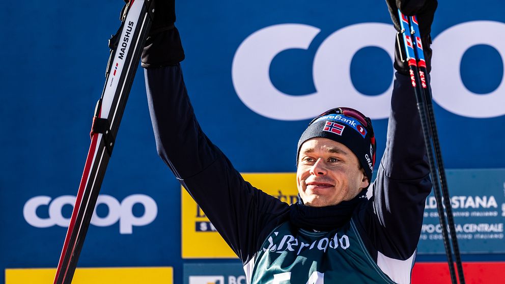 En skidåkare lyfter sina skidor i segergest mot en bakgrund med FIS Cross Country och Coop-loggor.