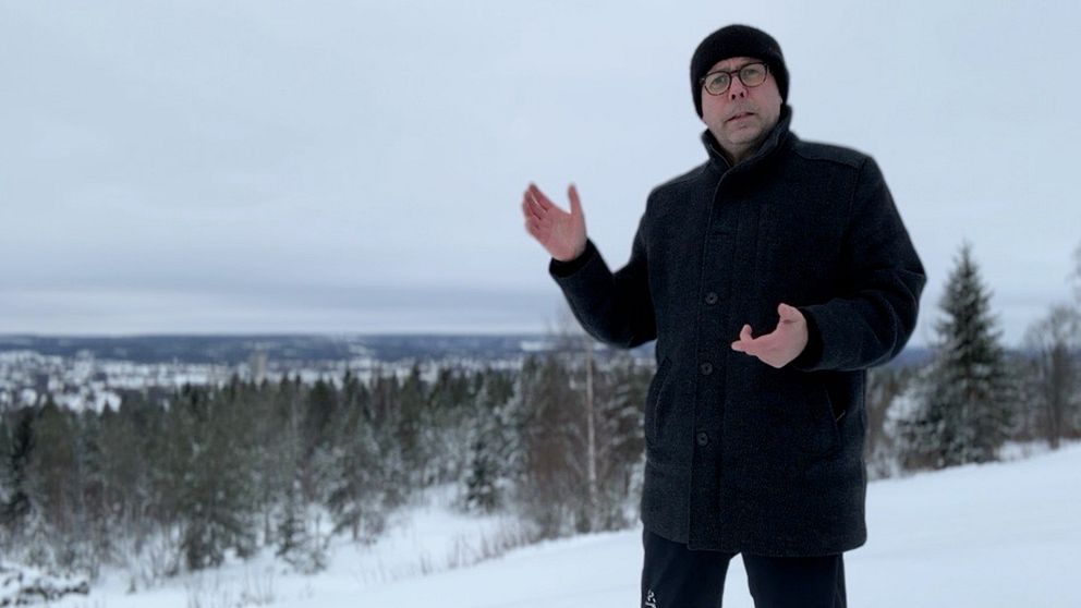 En reporter står med handen och visar i ett vinterlandskap