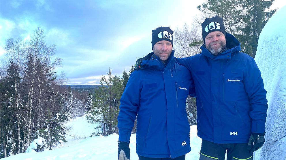 Två män i blåjackor upp på höjd med snöklädda vidder och vidsträckt utsikt