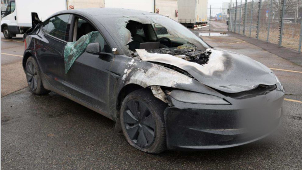 Kraftigt krockskadad svart personbil med bucklig motorhuv och krossat främre fönster.