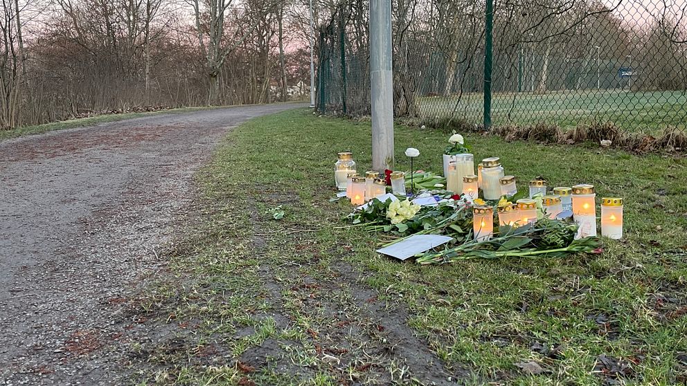 Minnesplats med ljus och blommor vid en parkstig.