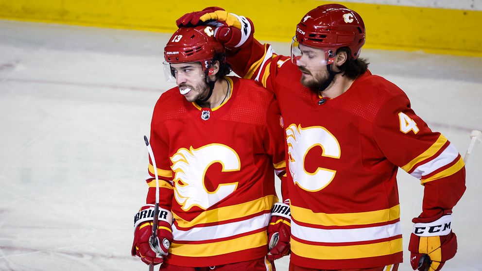 Två hockeyspelare i Calgary Flames firar ihop på isen i röda matchtröjor.