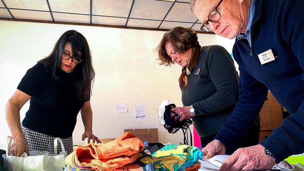 Tre personer från Rotaryklubben i Varberg står böjda över ett bord och packar kläder.