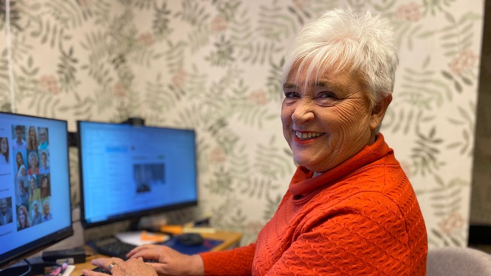 En kvinna, Helen Andersson, sitter i en röd klänning vid sin dator  som står på ett skrivbord.