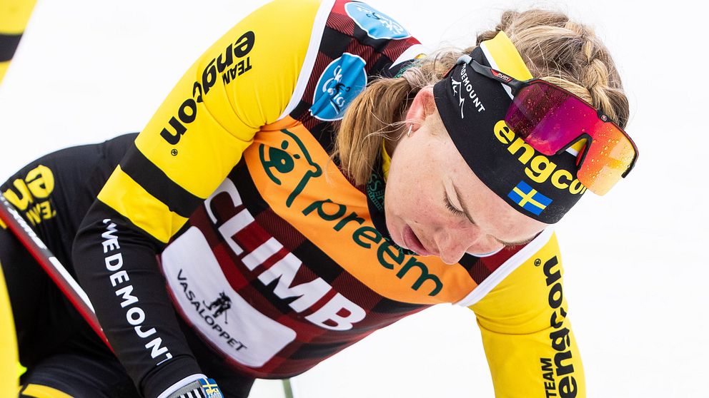 Ida Dahl sitter på snön efter ett lopp, med hjälpare bredvid sig.