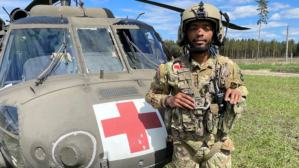 En ung man står i militära kläder framför en Blackhawk helikopter.