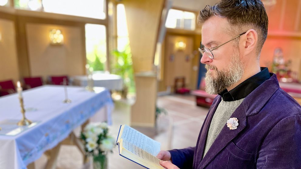 Man i kostym håller i en bok framför ett altare i en kyrka.