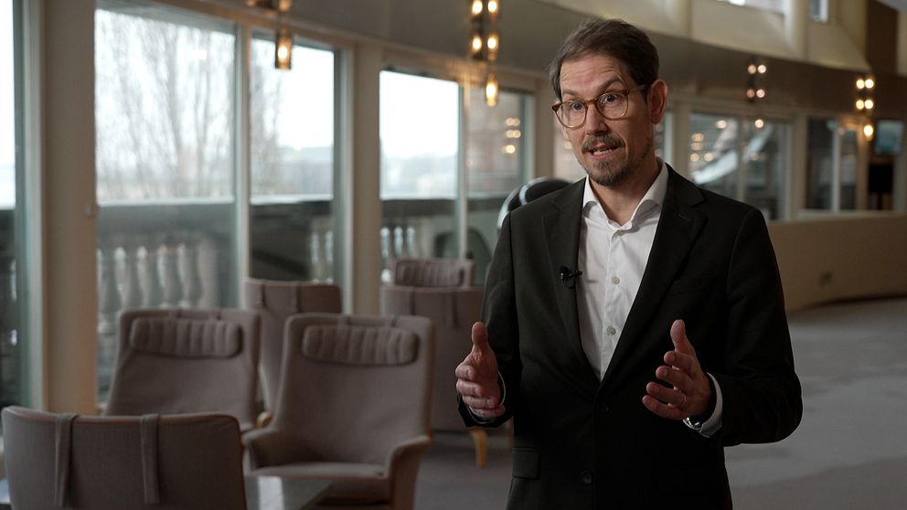 Niels Paarup-Petersen står i ett rum med stora fönster och tomma stolar.