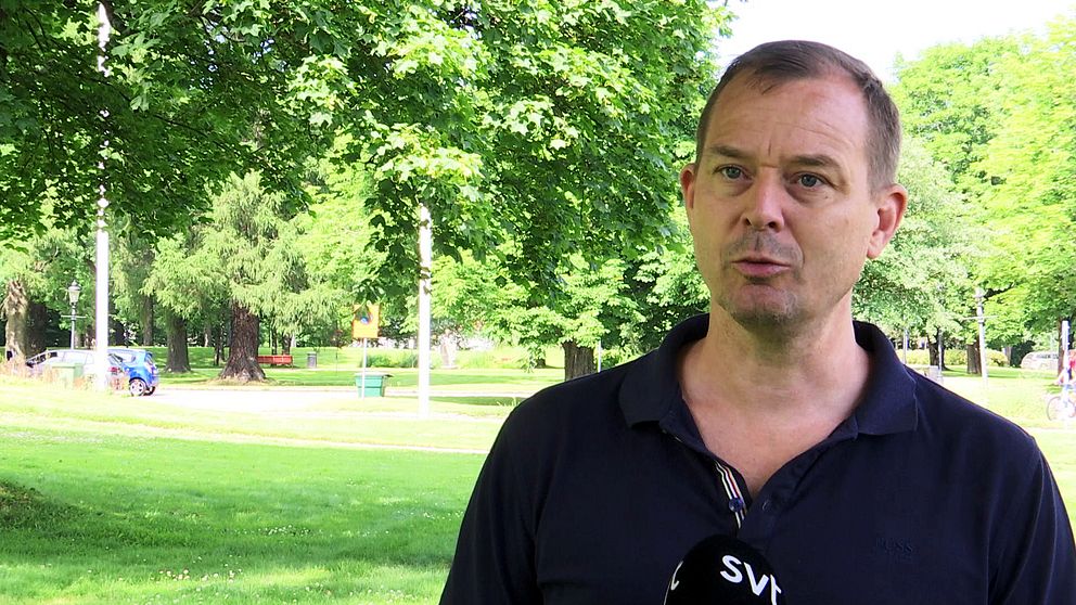 Magnus Lindström står i en grön park med träd och gräsmatta runt omkring. I bakgrunden syns en parkbänk och en lekplats. Han pratar i en mikrofon med en logotyp från SVT.