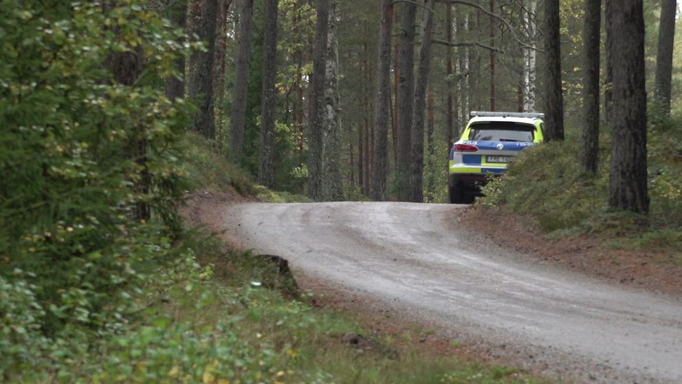Grusväg, en polisbil står parkerad i en kurva till höger i bild.