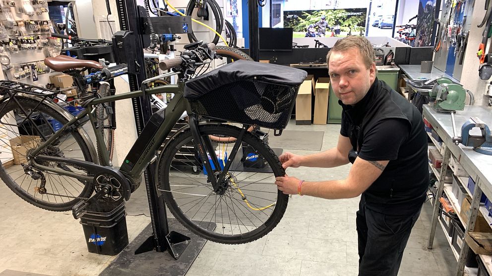 En cykel är upphissad på en verkstad, där Mikael Lipponen står och känner på framhjulet.